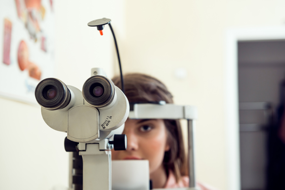 Portrait of cute caucasian female patient sitting in optometrist office, waiting for start of procedure to check her vision with microbioscope, sitting over yellow background. Ophthalmology concept